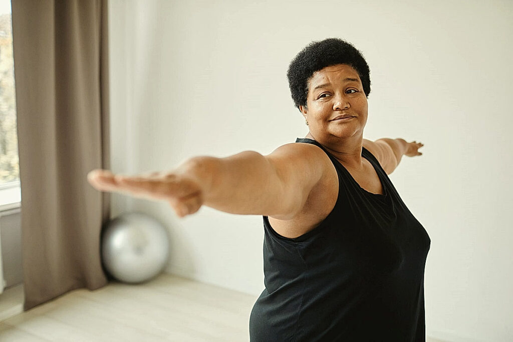 Yoga grandes tailles, une femme ouvre largement les bras dans une salle claire