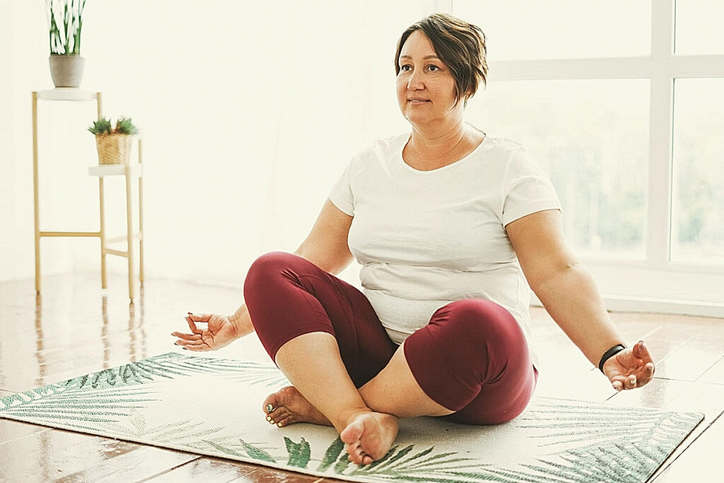 Yoga grandes tailles, une femme assise en tailleur sur un tapis, mains ouvertes
