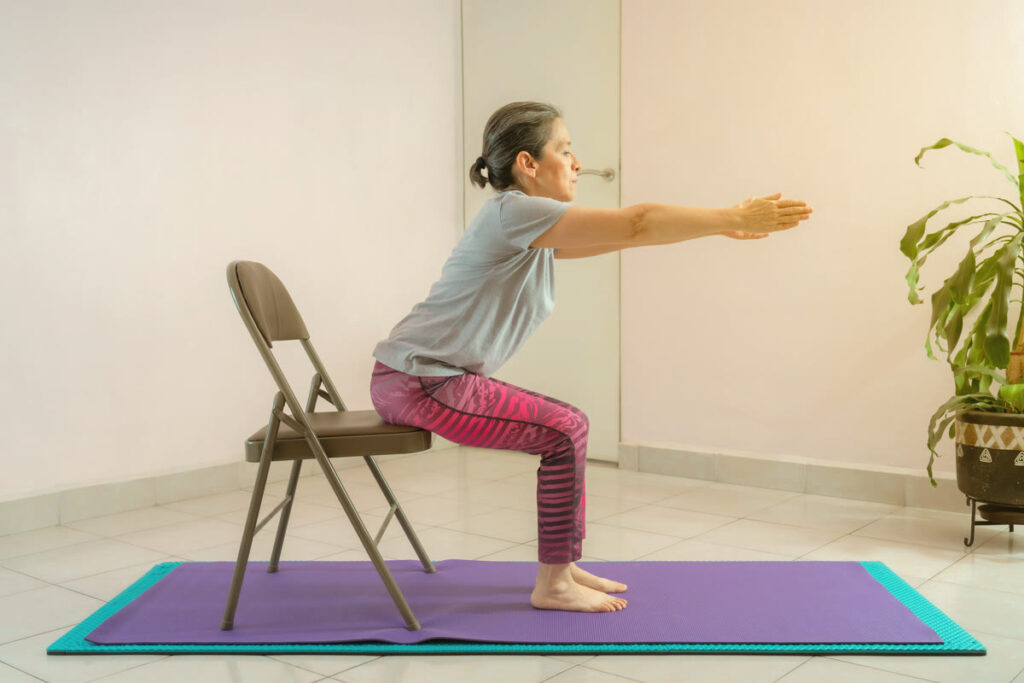 Femme âgée en assise sur une chaise, bras tendus devant elle, lors d'une pratique de yoga sur chaise.