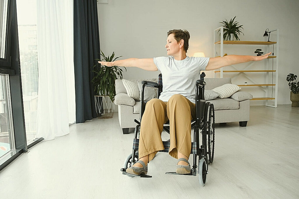 Femme assise en fauteuil roulant, bras ouverts, pratiquant le yoga sur chaise, un yoga accessible malgré les douleurs articulaires.
