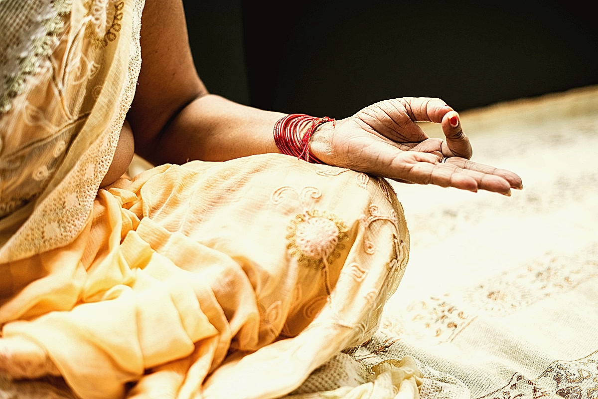 Main posée sur un genou en jnana mudra, sari abricot brodé et bracelets rouges