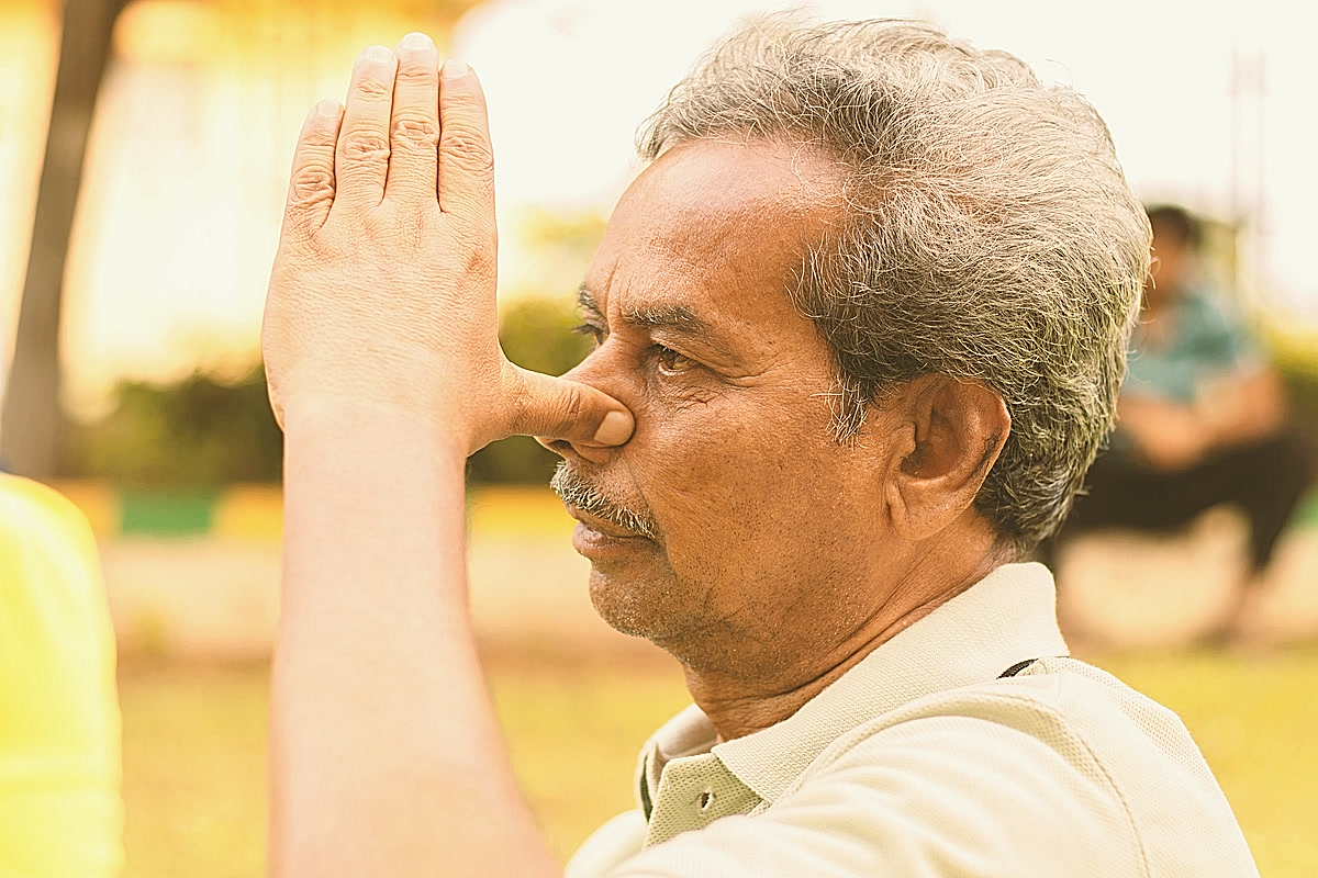 Homme aux cheveux gris pratiquant la respiration alternée, main posée contre le nez, vu de profil